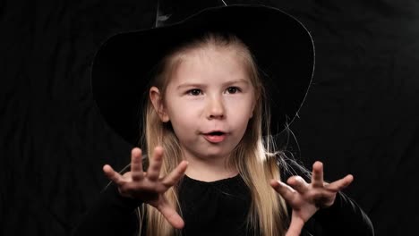 Little-pretty-girl-witch-in-black-dress-and-hat-screaming-at-dark-background