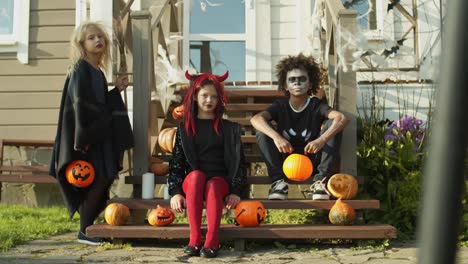 Three-Kids-in-Halloween-Costumes-Sitting-on-Porch