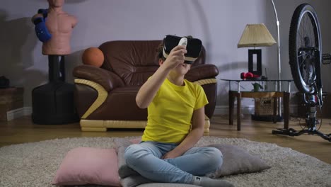 Young-Caucasian-teen-with-curly-hair-in-VR-headset-holding-remote-control-and-looking-around.-Child-using-virtual-reality.-Augmented-reality,-VR-glasses,-generation-Z.-Cinema-4k-ProRes-HQ.