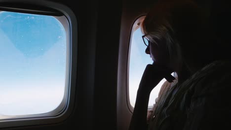 Eine-Frau-in-Gläsern-befasst-sich-mit-dem-Flugzeugfenster.-Silhouette,-Seitenansicht