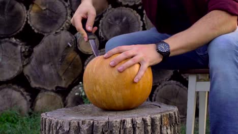 Man-carves-from-a-pumpkin-Jack-o'-lantern-in-the-backyard-on-a-tree-stump