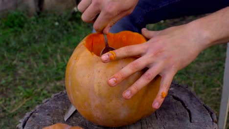 Man-carves-from-a-pumpkin-Jack-o'-lantern-in-the-backyard-on-a-tree-stump