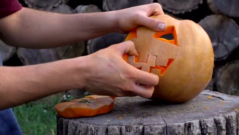 Man-carves-from-a-pumpkin-Jack-o'-lantern-in-the-backyard-on-a-tree-stump