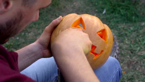 Man-carves-from-a-pumpkin-Jack-o'-lantern-in-the-backyard-on-a-tree-stump