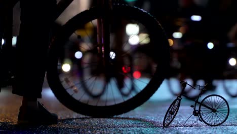 Lot-of-cyclists-ride-during-night-cycling-bike-parade-in-blur-by-illuminated-night-city-street-against-background-of-small-scale-model-of-bicycle-timalapse.-Crowd-of-people-on-bike.-Bike-traffic.-Concept-sport-healthy-lifestyle.-Bright-shining-lights.-Low