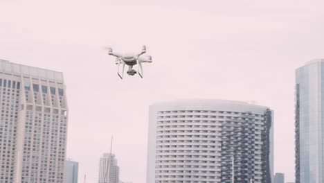 Quadrocopter-Drohne-mit-Kamera-auf-Gimbal-fliegen-in-den-Himmel-der-Stadt,-in-Zeitlupe-erschossen