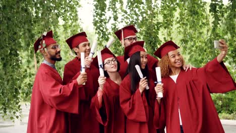 Muy-contentos-los-estudiantes-graduados-están-tomando-selfie-con-smartphone,-jóvenes-están-agitando-diplomas,-posando,-sonriendo-y-riendo.-Concepto-de-educación-y-el-éxito.