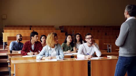 Tutor-ist-im-Gespräch-mit-Studenten-sitzen-am-Schreibtisch-im-geräumigen-College-Hörsaal,-junge-Menschen-in-Freizeitkleidung-stellen-Fragen.-Bildung-und-Hochschule-Konzept.