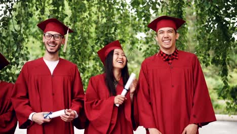 Slow-motion-portrait-of-graduating-students-standing-in-line-holding-diplomas-and-laughing-looking-at-camera.-Girls-and-guys-are-wearing-mortar-boards-and-gowns.