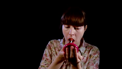 Young-woman-is-applying-red-lipstick-on-her-lips-against-a-black-background.