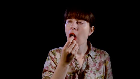 Young-woman-is-applying-red-lipstick-on-her-lips-against-a-black-background.