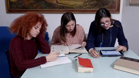 Tres-alumnas-estudiando-libros-de-Alasdair,-dispositivos,-aprendizaje