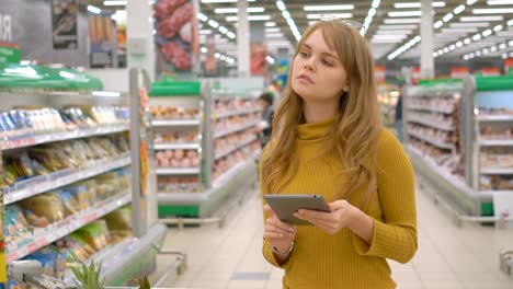 Women-shopping-at-the-supermarket-and-using-mobile-apps-on-her-tablet