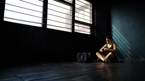 Panning-young-beautiful-woman-sitting-on-floor-and-wrapping-hands-with-black-boxing-wraps-in-club.