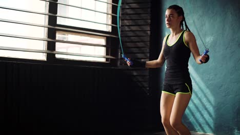 Young-purposeful-serious-female-boxer-in-wrapped-bandage-fist-hands-jumping-on-skipping-rope-in-gym