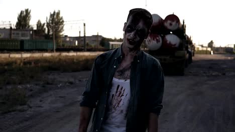 Creepy-zombie-man-with-clawing-hands-walking-outdoors-with-an-industrial-abandoned-place-on-the-background.-Halloween,-filming,-creepy-concept