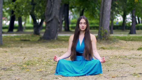 Schöne-Frau-im-blauen-Kleid-in-Lotus-stellen-meditieren-im-Park,-langsame-Dolly-Pfanne