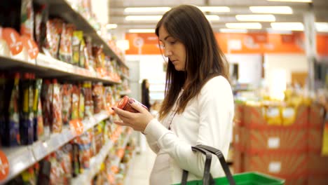 Mujer-joven-de-pie-en-una-botella-de-ketchup-en-las-manos-de-un-supermercado.-El-feliz-comprador-hace-las-compras-en-el-supermercado.