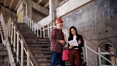 Construction-worker-and-engineer-talking-in-the-stairwell-at-construction-site.-Workers-in-helmets-at-building-area.