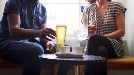 Mid-section-close-up-of-couple-in-conversation,-sitting-with-drinks-at-a-window-seat-in-a-pub,-slow-motion