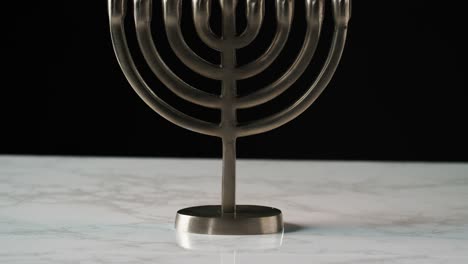 Inclinación-de-tiro-del-candelabro-menorah-judía-con-velas-encendidas-sobre-una-superficie-de-mármol-gris-sobre-fondo-negro