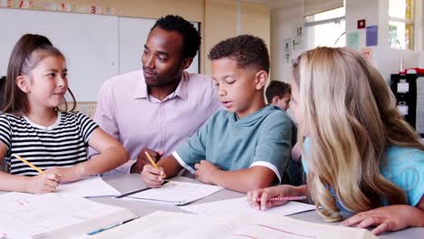 Profesor-de-la-escuela-primaria-masculina-viene-a-kidsÍ-escritorio-para-ayudar-a