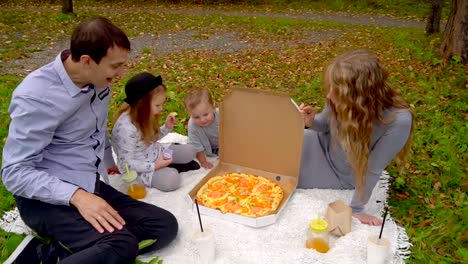 Familie-im-Herbst-Park-Essen-Pizza-auf-dem-Rasen