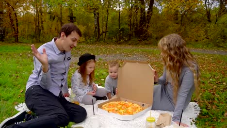 Familie-im-Herbst-Park-Essen-Pizza-auf-dem-Rasen