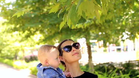 Una-joven-madre-feliz-camina-con-su-hijo-recién-nacido-en-el-parque-en-verano.