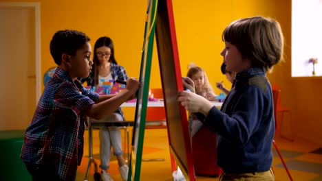 Diverse-boys-drawing-and-painting-on-easel-board