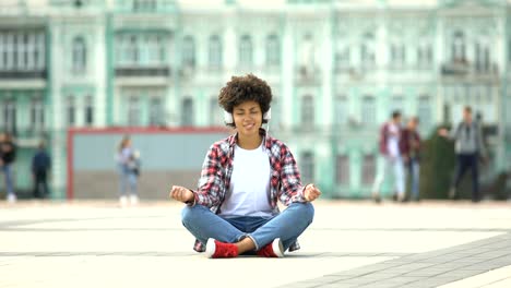 Carefree-young-female-sitting-in-lotus-pose-and-listening-to-music-in-headphones