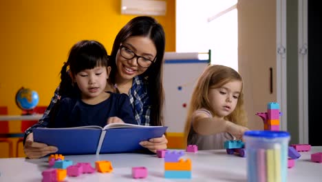 Preschool-asian-girl-reading-book-with-teacher