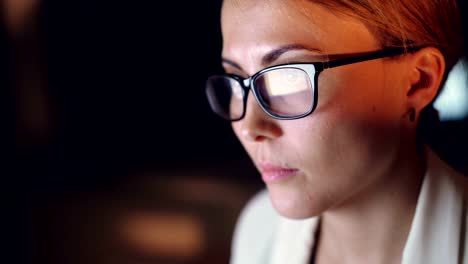 Headshot-of-attractive-young-businesswoman-working-late-at-night-in-office-alone,-a-reflection-of-computer-screen-is-visible-in-her-glasses.-People-and-job-concept.