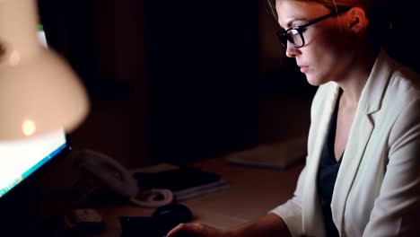 Tilt-down-shot-of-pretty-young-business-woman-working-on-computer-late-at-night-typing-using-keyboard-sitting-at-desk-alone.-Overtime-job-and-career-concept.