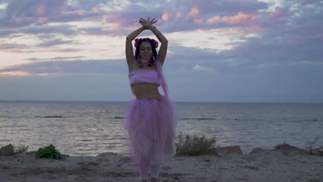 Tender-young-woman-with-sparkling-makeup-in-a-pink-dress-dancing-on-the-bank-of-the-river.-The-dance-of-a-sweet-sensual-lady-with-a-flower-hairstyle.-Slow-motion.