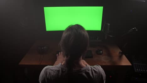 A-man-with-long-hair-prints-text-on-his-keyboard,-he-has-a-green-screen-on-his-monitor.-4K-Slow-Mo