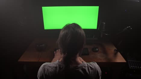 Un-hombre-con-pelo-largo-imprime-texto-en-su-teclado,-tiene-una-pantalla-verde-en-su-monitor.-4K-Slow-mo