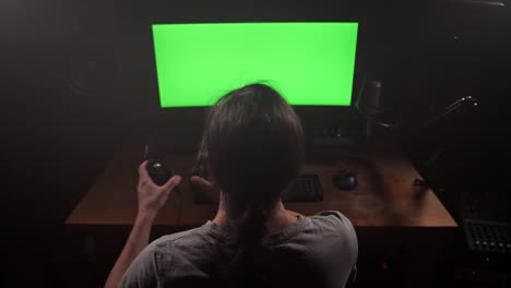 A-man-in-headphones-looks-at-the-green-screen-of-the-monitor,-removes-the-headphones,-looks-at-the-screen,-starts-typing.-4K-Slow-Mo