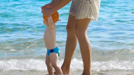 De-vacaciones-una-mamá-da-los-primeros-pasos-a-su-pequeño-bebé-en-la-playa-paso-a-paso-el-recién-nacido-aprende-a-caminar...