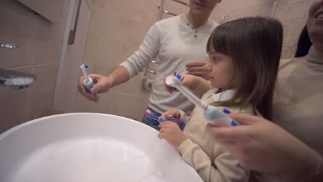 Morning-Hygiene,-young-mother-and-daddy-teaching-child-girl-with-toothbrush-brush-teeth-in-front-of-mirror