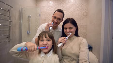 familia-cepillarse-los-dientes,-la-niña-encantadora-con-los-padres-con-cepillo-de-dientes-cepillarse-el-diente-delante-del-espejo