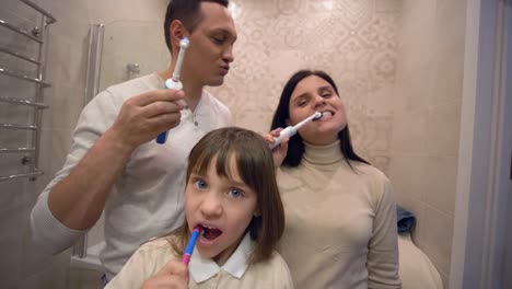 Peluquería-matutina,-niña-sana-con-familia-con-cepillo-de-dientes-en-la-parte-frontal-del-espejo