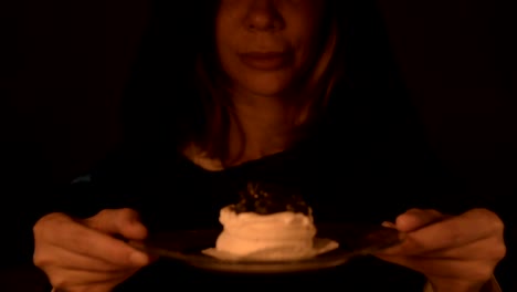 Close-up-of-a-contented-girl-magician-in-a-dark-room-by-candlelight-conjured-herself-a-cake.-Holds-a-plate-of-cake-Low-key-live-camera.
