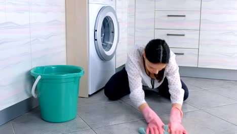 Tired-woman-in-pink-rubber-gloves-washes-kitchen-floor-with-a-cloth-and-looks-at-camera.