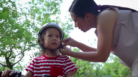 Mother-helping-her-son-(Long-hair-boy)--to-put-on-bicycle-helmet-outdoors.