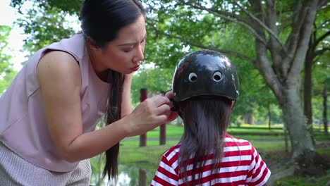 Madre-ayudando-a-su-hijo-(niño-de-pelo-largo)-a-ponerse-el-casco-de-la-bicicleta-al-aire-libre.