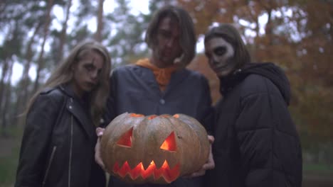 Tall-handsome-man-holding-Halloween-pumpkin-with-a-light-inside,-two-pretty-girls-standing-near.