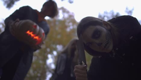 Hombre-y-dos-mujeres-con-trajes-de-Halloween-mirando-a-la-víctima-con-caras-de-miedo-serios-en-el-parque-de-otoño.