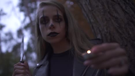 Pretty-blonde-psycho-girl-with-horrifying-Halloween-make-up-holding-hatchet-and-small-candle-in-hands