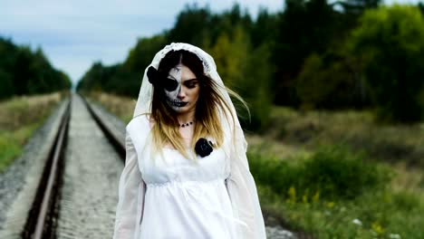 Halloween.-Eine-Frau-mit-gruseligem-Make-up,-die-auf-den-Schienen-im-Wald-spazieren-geht.-4K